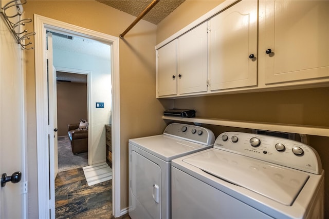 clothes washing area with cabinets, a textured ceiling, and washing machine and clothes dryer