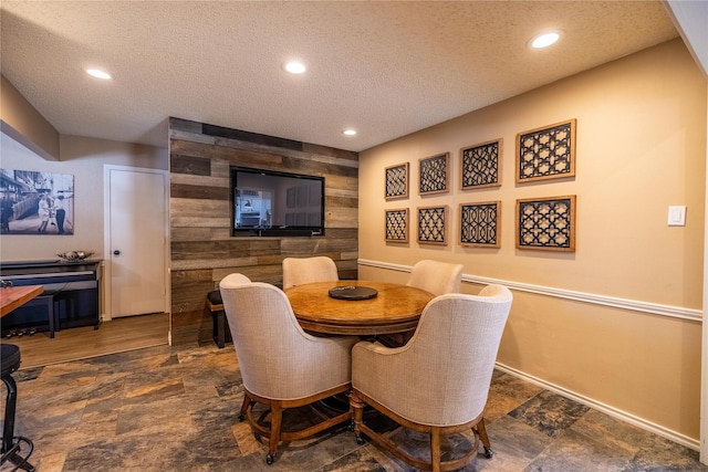 dining space featuring a textured ceiling and wood walls