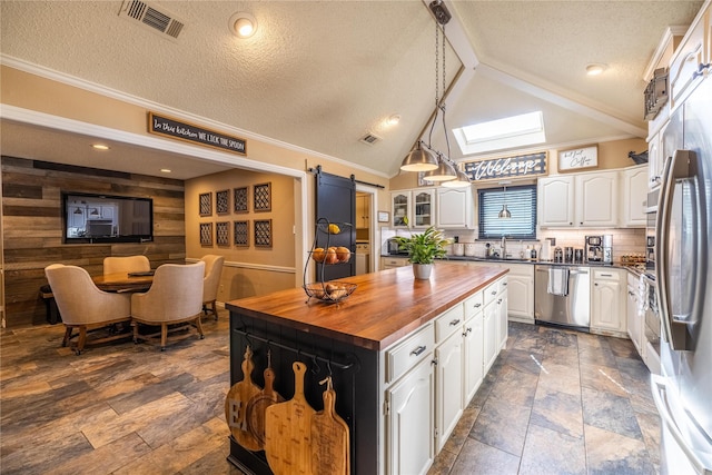 kitchen featuring appliances with stainless steel finishes, vaulted ceiling with skylight, white cabinets, a barn door, and wood walls