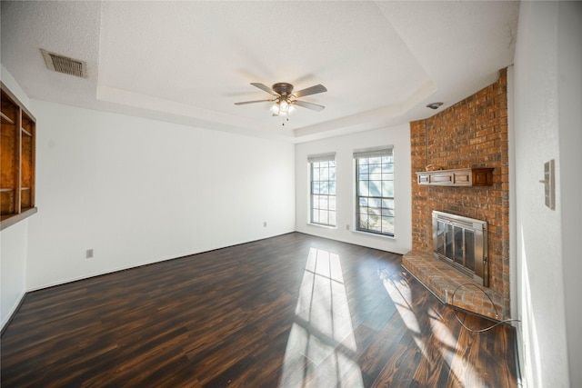 unfurnished living room with a textured ceiling, a fireplace, dark hardwood / wood-style floors, ceiling fan, and a tray ceiling