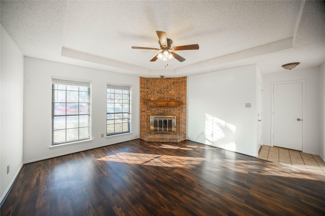 unfurnished living room featuring a textured ceiling, dark hardwood / wood-style flooring, a raised ceiling, and a fireplace