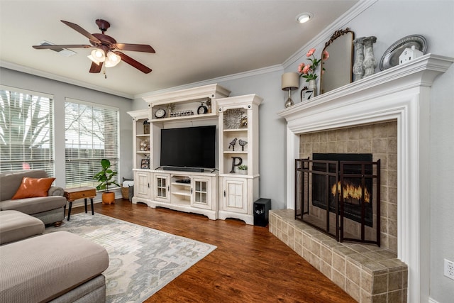 living room with crown molding, a tiled fireplace, dark wood-type flooring, and ceiling fan