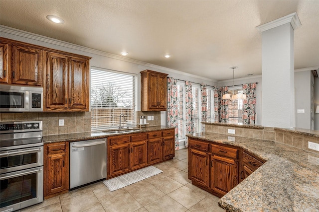 kitchen featuring crown molding, hanging light fixtures, appliances with stainless steel finishes, sink, and light stone countertops