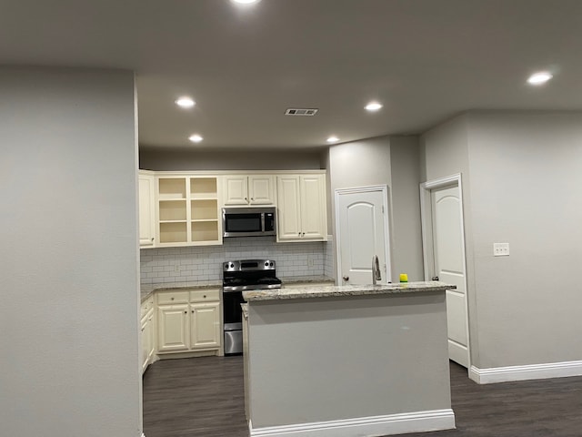 kitchen with decorative backsplash, white cabinets, appliances with stainless steel finishes, and an island with sink