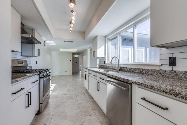 kitchen with white cabinets, wall chimney range hood, sink, backsplash, and stainless steel appliances