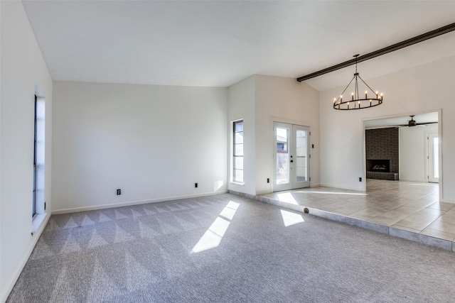 unfurnished living room featuring ceiling fan with notable chandelier, light carpet, french doors, vaulted ceiling with beams, and a brick fireplace