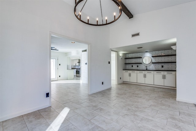 unfurnished living room featuring sink, high vaulted ceiling, beam ceiling, and an inviting chandelier