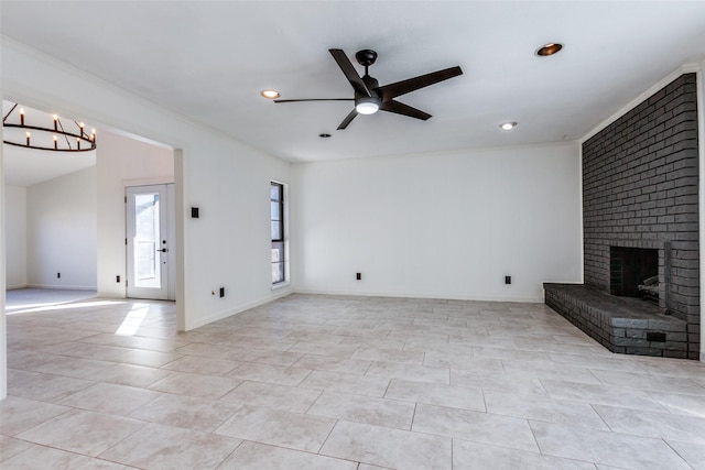 unfurnished living room with ceiling fan with notable chandelier and a brick fireplace