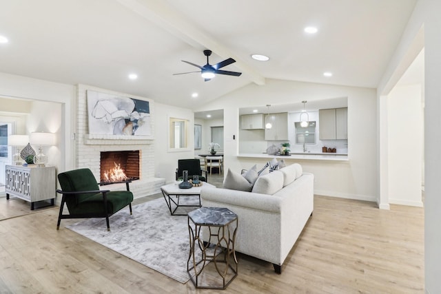 living room with a fireplace, light wood-type flooring, vaulted ceiling with beams, and ceiling fan