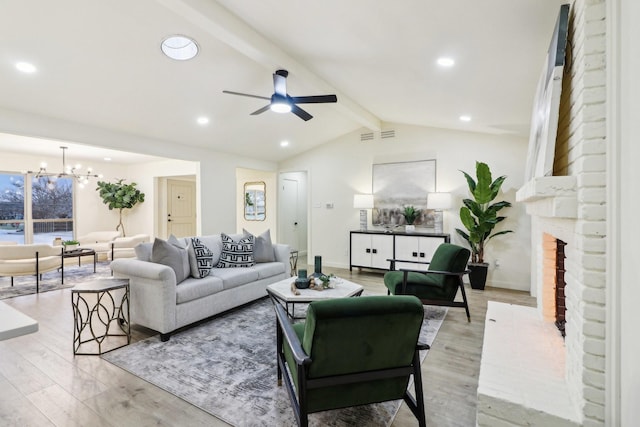 living room with a fireplace, ceiling fan with notable chandelier, lofted ceiling with beams, and light hardwood / wood-style flooring