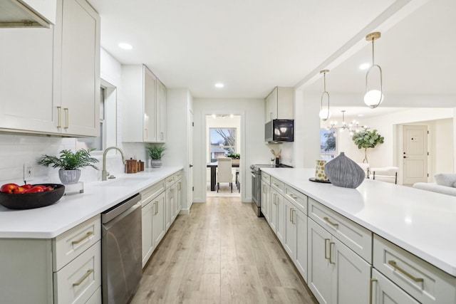 kitchen with appliances with stainless steel finishes, sink, decorative light fixtures, backsplash, and light wood-type flooring