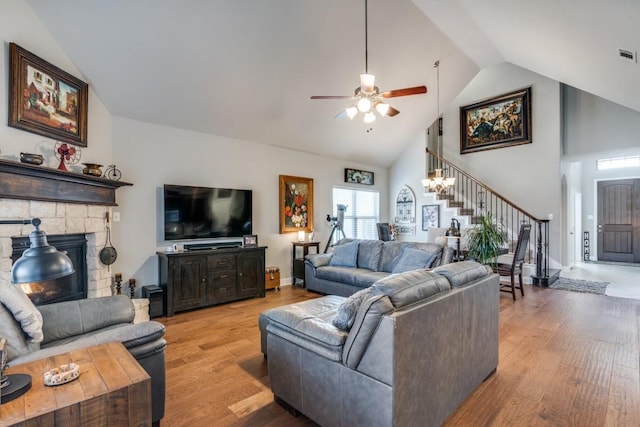 living room featuring a stone fireplace, high vaulted ceiling, and light hardwood / wood-style flooring