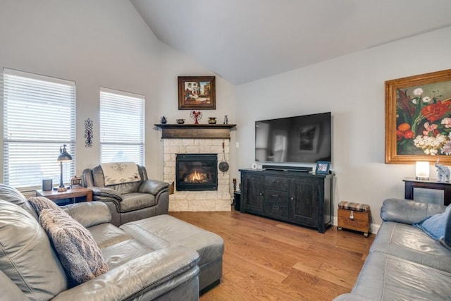 living room with a stone fireplace, vaulted ceiling, and light wood-type flooring