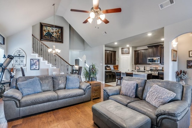 living room with sink, ceiling fan with notable chandelier, high vaulted ceiling, and light hardwood / wood-style flooring