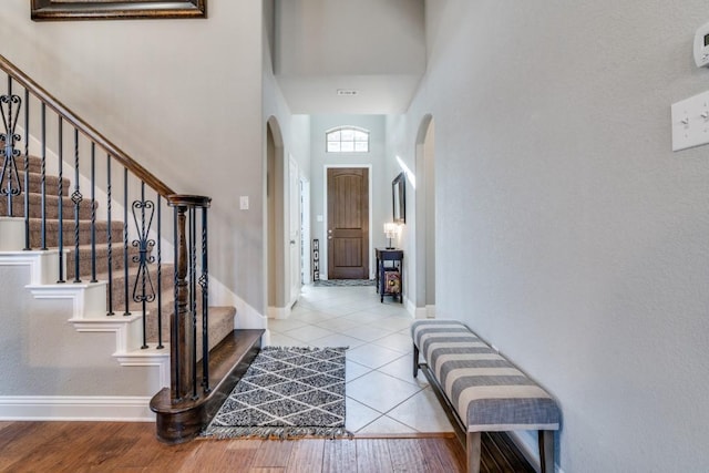 foyer with tile patterned flooring, baseboards, stairs, a high ceiling, and arched walkways