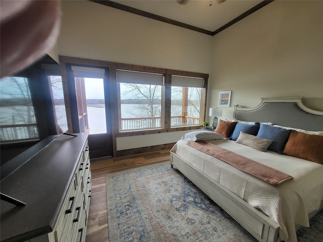 bedroom with crown molding, hardwood / wood-style flooring, a water view, and multiple windows