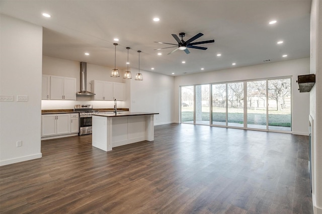 kitchen featuring wall chimney exhaust hood, white cabinetry, hanging light fixtures, a center island with sink, and stainless steel range with gas stovetop