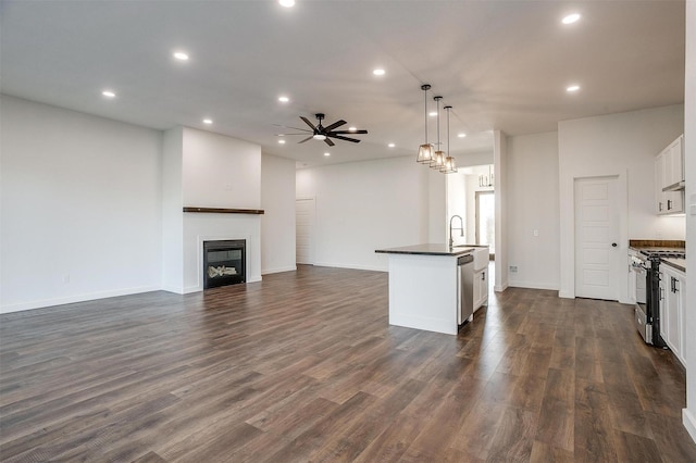 kitchen with white cabinets, appliances with stainless steel finishes, dark wood-type flooring, hanging light fixtures, and a kitchen island with sink