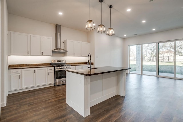 kitchen featuring decorative light fixtures, white cabinets, wall chimney range hood, a center island with sink, and gas stove