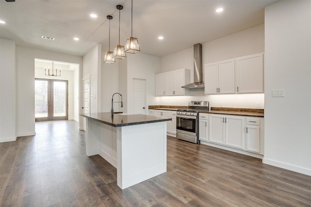 kitchen featuring white cabinets, wall chimney exhaust hood, french doors, an island with sink, and stainless steel range with gas cooktop