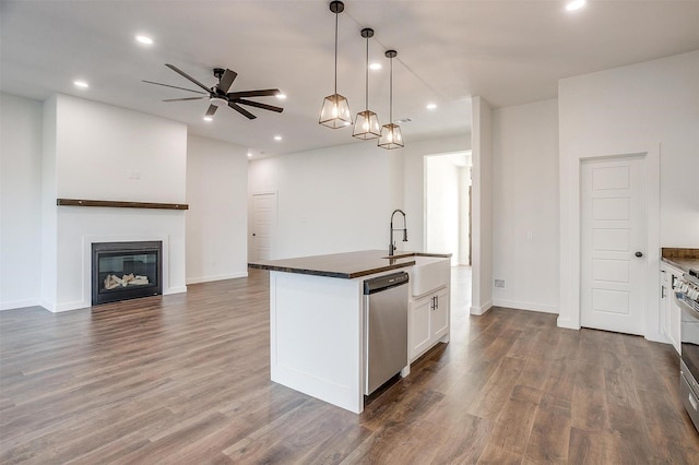 kitchen with decorative light fixtures, dark wood-type flooring, white cabinetry, a center island with sink, and stainless steel appliances