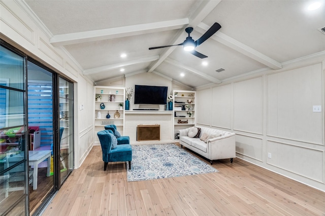 living room featuring vaulted ceiling with beams, built in features, ornamental molding, ceiling fan, and light hardwood / wood-style flooring