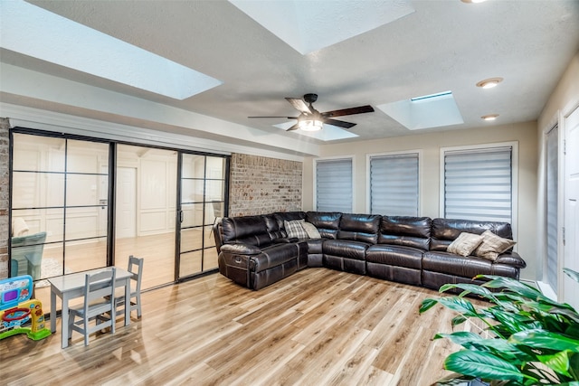 living room featuring a textured ceiling, light hardwood / wood-style flooring, a skylight, and ceiling fan