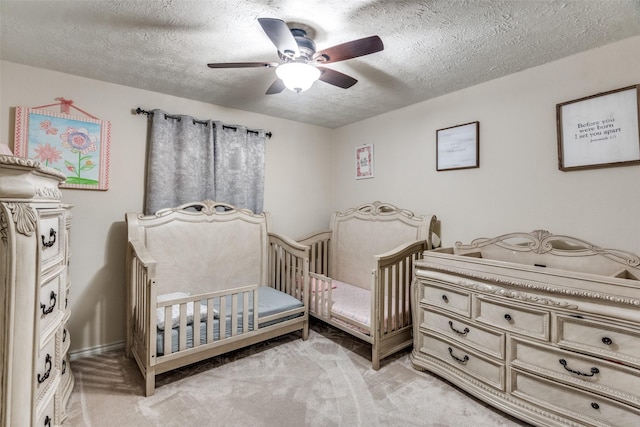 bedroom featuring a crib, a textured ceiling, light colored carpet, and ceiling fan