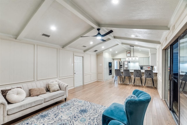 living room with ceiling fan, light wood-type flooring, lofted ceiling with beams, a textured ceiling, and ornamental molding