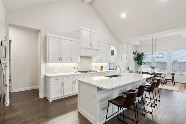 kitchen featuring an island with sink, stainless steel gas cooktop, white cabinets, and decorative light fixtures