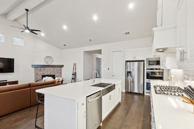 kitchen with white cabinets, stainless steel appliances, an island with sink, and backsplash