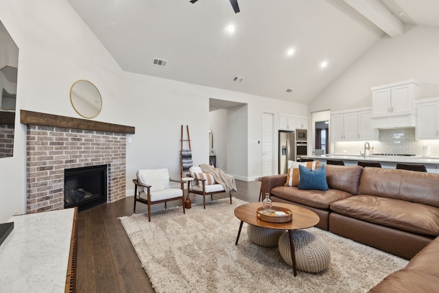 living room with ceiling fan, high vaulted ceiling, dark hardwood / wood-style flooring, a brick fireplace, and beamed ceiling