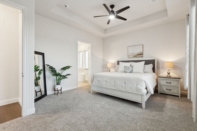 carpeted bedroom featuring a raised ceiling, ceiling fan, and ensuite bath