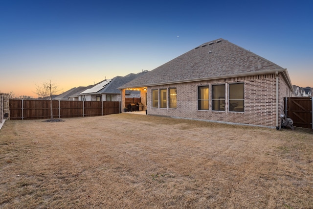 back house at dusk featuring a lawn