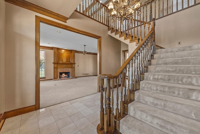 stairs featuring a towering ceiling, a fireplace, ornamental molding, a notable chandelier, and carpet flooring