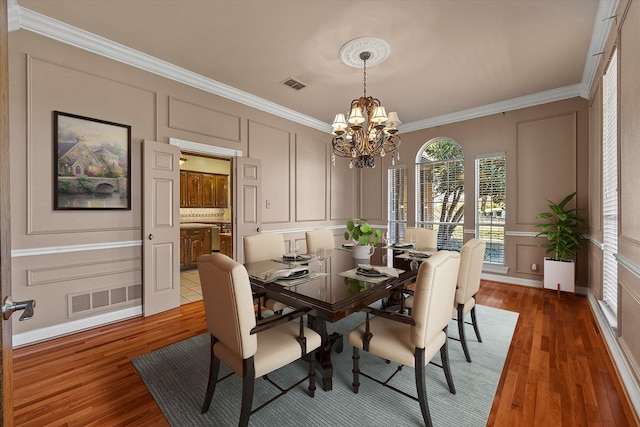 dining space with hardwood / wood-style flooring, crown molding, and a chandelier