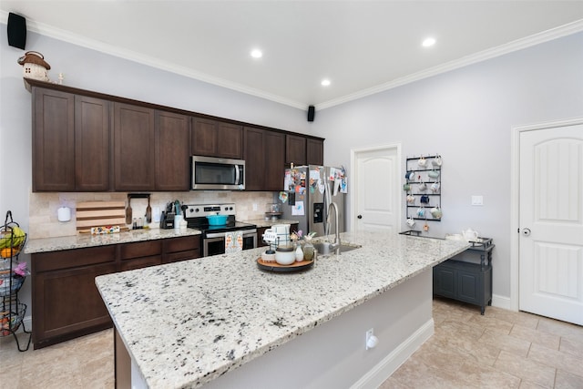 kitchen with light stone counters, ornamental molding, an island with sink, and appliances with stainless steel finishes