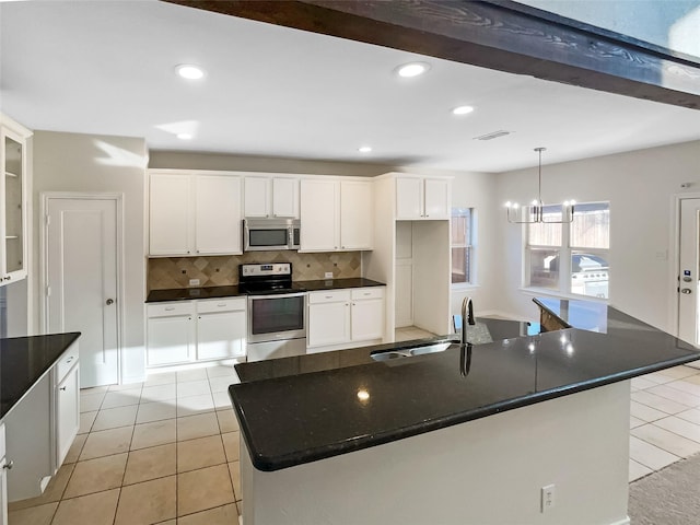 kitchen featuring an island with sink, tasteful backsplash, white cabinetry, and appliances with stainless steel finishes