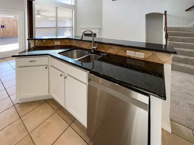 kitchen with stainless steel dishwasher, white cabinetry, dark stone counters, sink, and light tile patterned floors