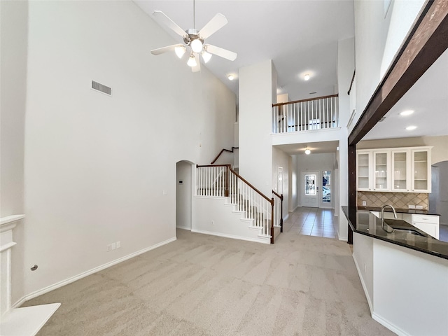 unfurnished living room with ceiling fan, a high ceiling, light carpet, and sink