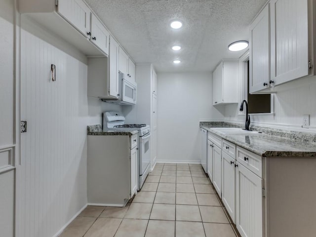 kitchen with sink, white appliances, white cabinetry, a textured ceiling, and light tile patterned flooring