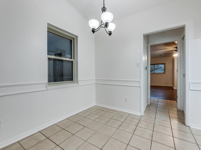 tiled spare room with ceiling fan with notable chandelier