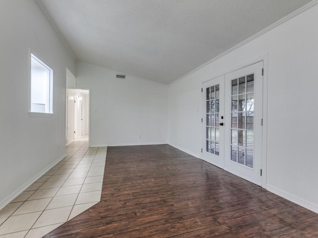 spare room with lofted ceiling, ornamental molding, light hardwood / wood-style floors, a textured ceiling, and french doors