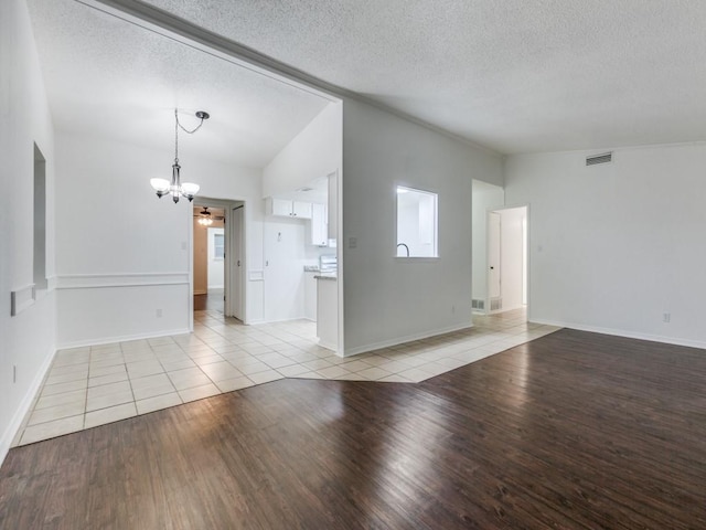 empty room featuring ceiling fan with notable chandelier, vaulted ceiling, light hardwood / wood-style floors, and a textured ceiling