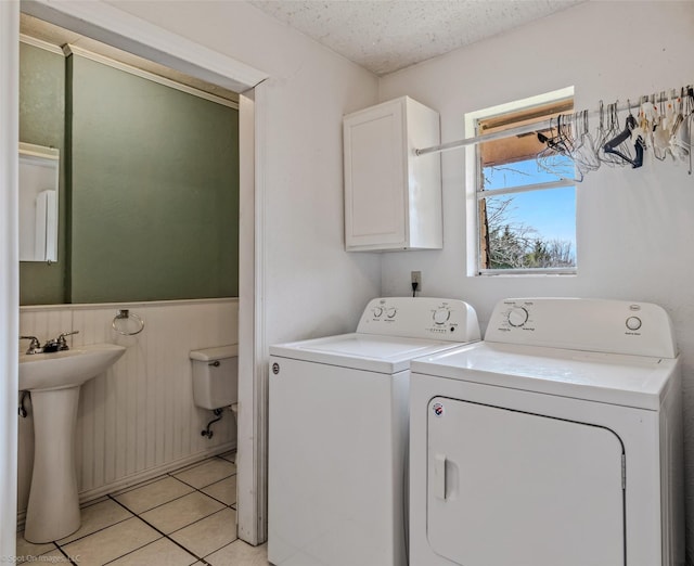 clothes washing area featuring a textured ceiling, washing machine and clothes dryer, light tile patterned floors, sink, and cabinets