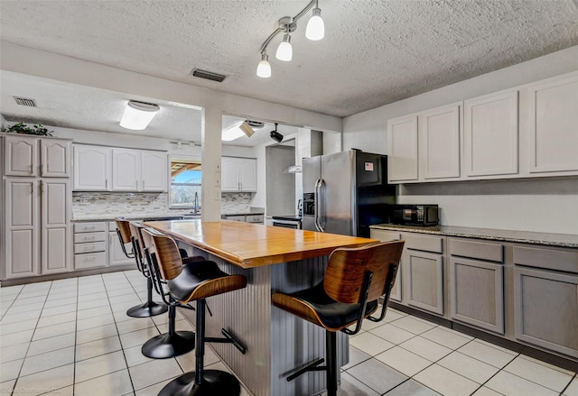 kitchen featuring sink, rail lighting, stainless steel fridge, gray cabinets, and a breakfast bar area