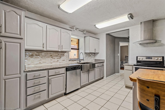 kitchen with appliances with stainless steel finishes, sink, light stone counters, light tile patterned flooring, and wall chimney range hood