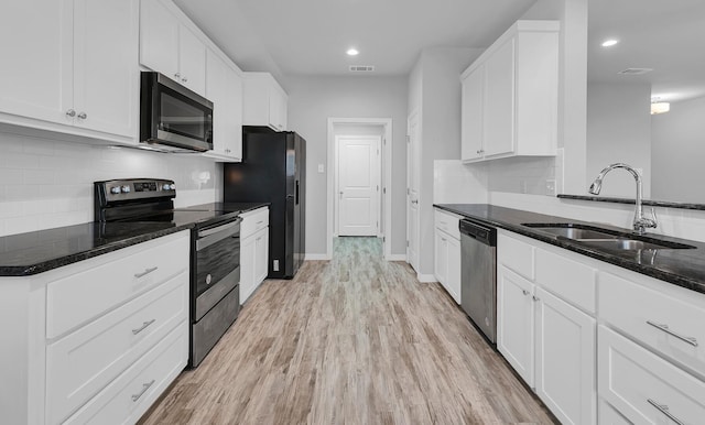 kitchen featuring appliances with stainless steel finishes, white cabinetry, dark stone counters, light hardwood / wood-style floors, and sink