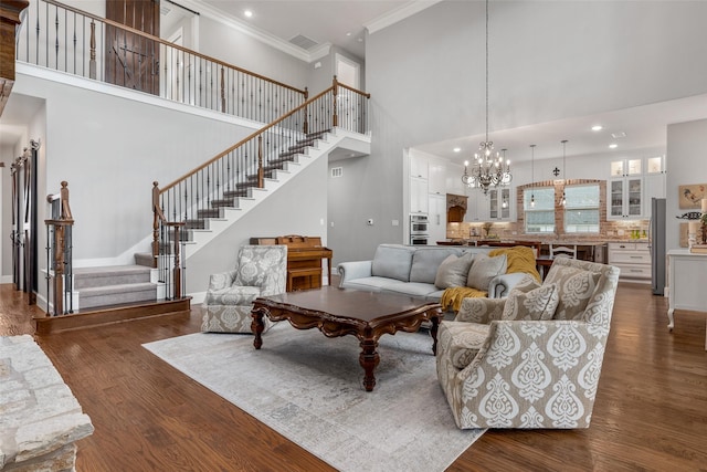 living room with crown molding, a towering ceiling, dark hardwood / wood-style floors, and an inviting chandelier