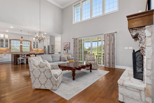 living room with a stone fireplace, an inviting chandelier, ornamental molding, dark hardwood / wood-style flooring, and a high ceiling